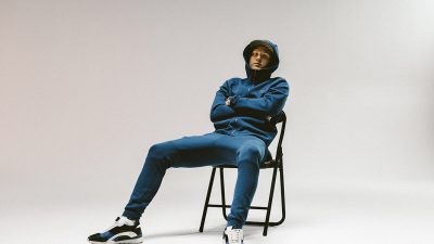 Rapparen Einár sitter i en stol. Han har en jacka med luvan uppdragen.